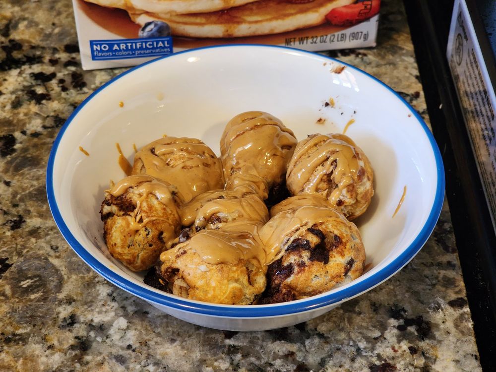 A bowl of what looks like takoyaki but is actually pancake balls topped with peanut butter and syrup.