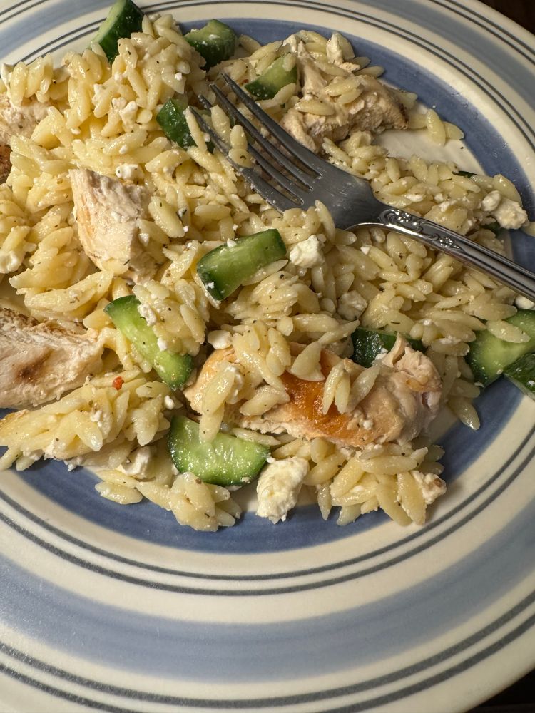 A plate of orzo mixed with diced chicken, cucumbers, and feta cheese, with a fork resting on the side.