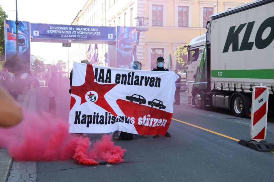 Sponti mit pinkem Rauch, einem Transparent „IAA entlarven, Kapitalismus stürzen“ beim Aufbau des Open Space am Wittelsbacherplatz