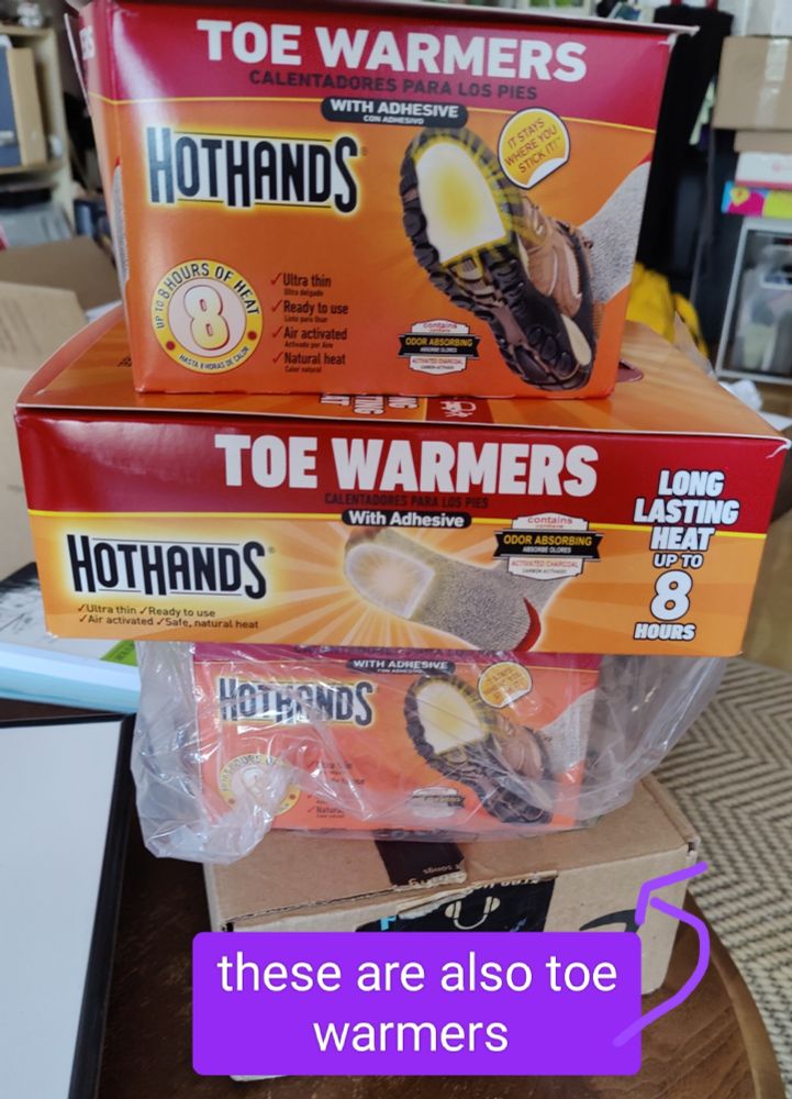 Four stacked boxes, one an Amazon box and three others labeled HOT HANDS. All four are filled with toe warmers.