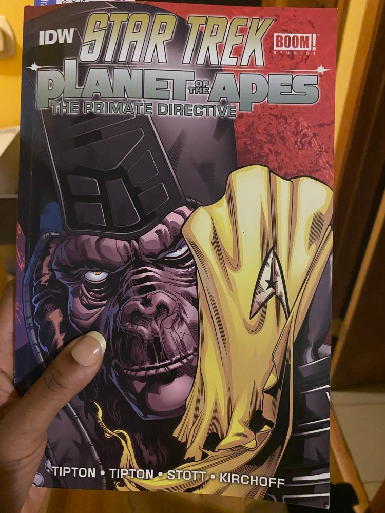 Black women’s french manicured & moisturized hand holding “The Primate Directive” comic