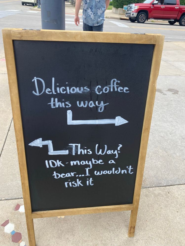 Chalk sign in front of a cafe with an arrow pointing to the cafe for delicious coffee and the other “IDK maybe a bear”