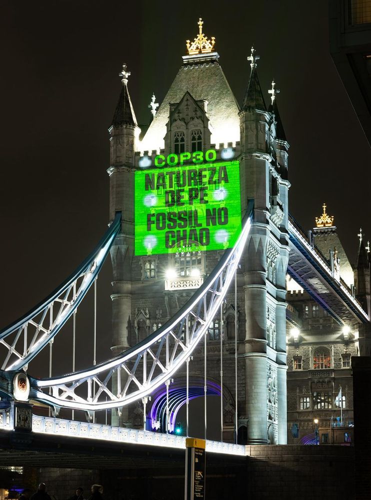 Photo of green projection on the Tower bridge reading “COP30 NATUREZA DE PE FOSSIL NO CHÃO”