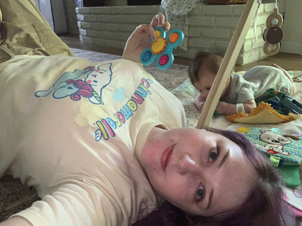 Me laying on the floor next to my baby nephew on his play mat. I am holding a color fidget spinner of sorts for babies