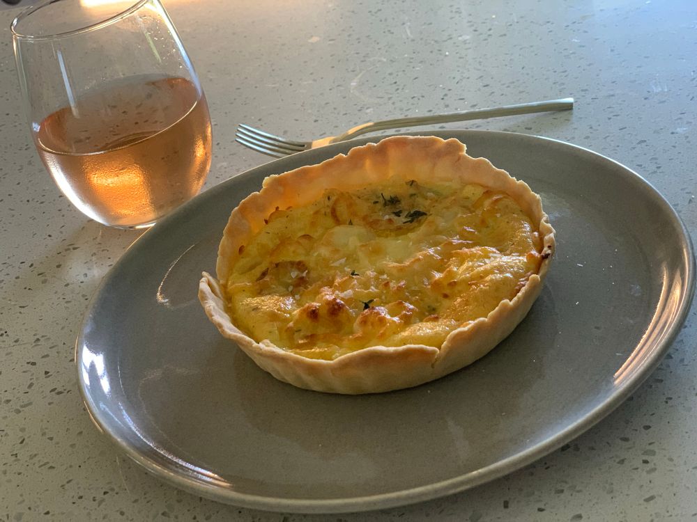 Aesthetic pic of my lunch. An un-shelled quiche on a plate next to a glass of rosé
