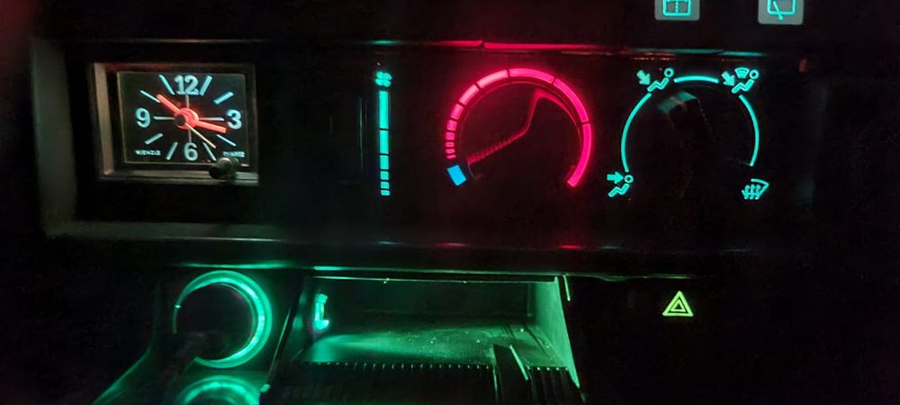 The analogue clock of a 1988 Renault 5 TR, lit up in the wonderful neon teal-green glow from the backlit dashboard illumination at night.

The clock was a stand-out feature of the TR trim level! It was only an optional extra on all the trim levels below it, where there'd just be a tiny cubby hole there instead. Useful only for storing the clothes peg you use to keep the choke lever out!