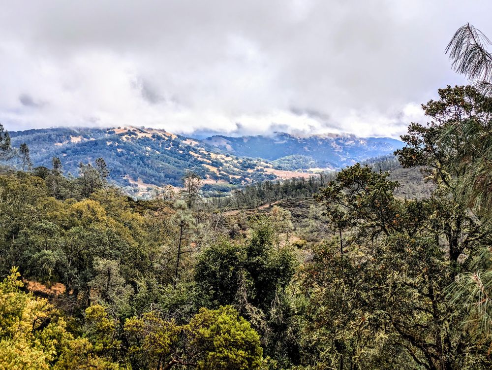 View over the hills to a valley and the distance with a cloudy sky above.
