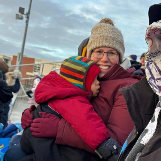 Not a selfie, but a rare photo of me holding my youngest, a toddler, while sitting in a football stadium. We're both bundled up in lots of layers. I have a big grin and a gigantic toque.