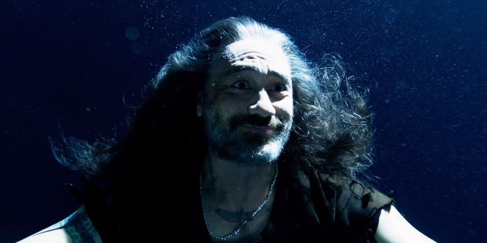 ed teach floating in the sea, smiling as the greatest wig in the history of television wistfully hovers in the water around him, with the pearls around his neck as ed smiles because the man he loves has come to save his life (our flag means death s2e3)