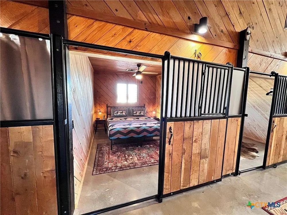 A stables-like room with a human bed and rug and vaguely trans-colored blanket on the bed