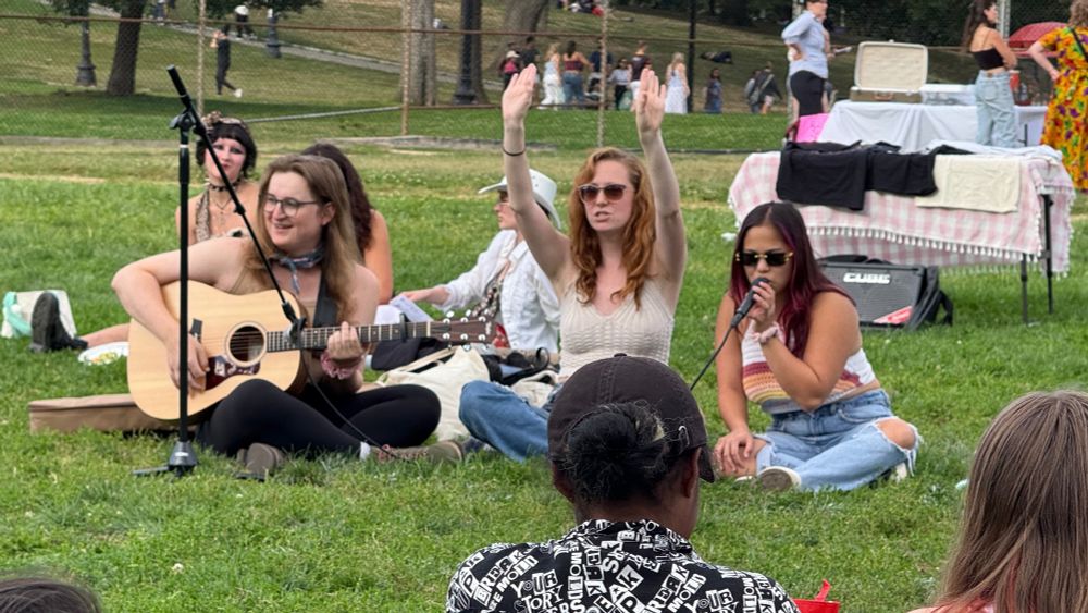 Ellie, Bailey, and Vee playing guitar and singing (leading a sing-along) on Boston Common at Camp Lesbos