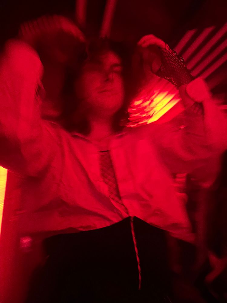 Milk dancing in the goth club, red lighting, lost in her own world with messy hair