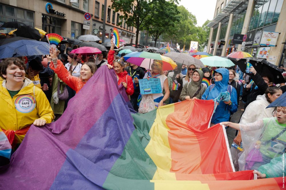 Menschen auf CSD Demo mit großer Regenbogenflagge