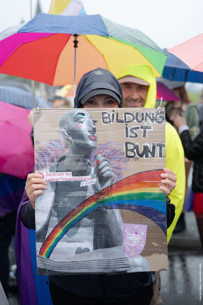Mensch mit Plakat auf CSD Demo mit Schriftzug "Bildung ist Bunt", Regenbogenschirm