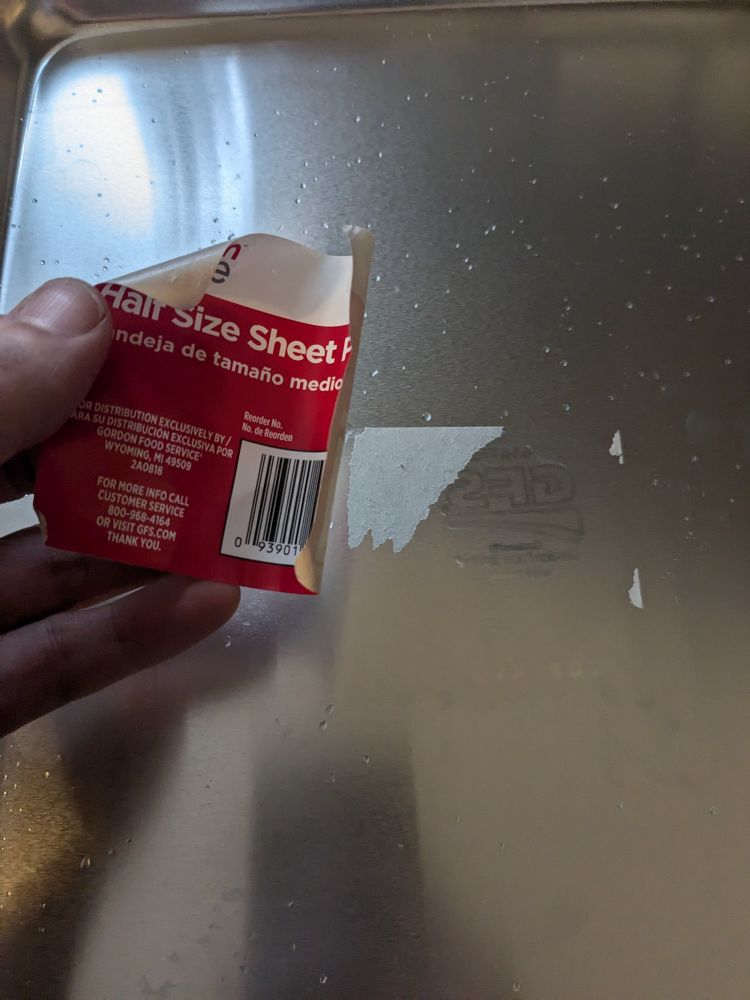 A metal sheet pan with the retail sticker peeled off. Some of the sticker has remained on the pan, much to the poster's consternation.