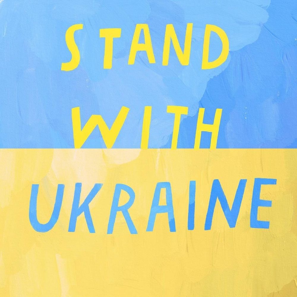 The blue and yellow flag of Ukraine with the words “I Stand With Ukraine@

