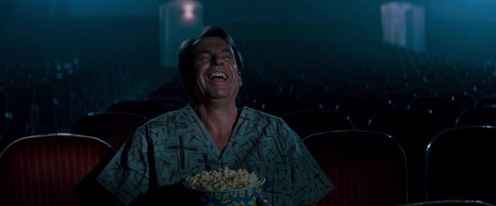 Still from In the Mouth of Madness of a man sitting in a theater by himself and laughing hysterically 