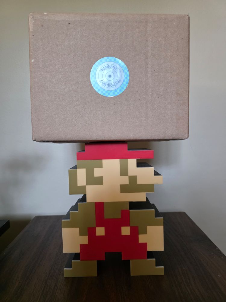 8-bit Mario balances a Remnant Controllers box on his head. 