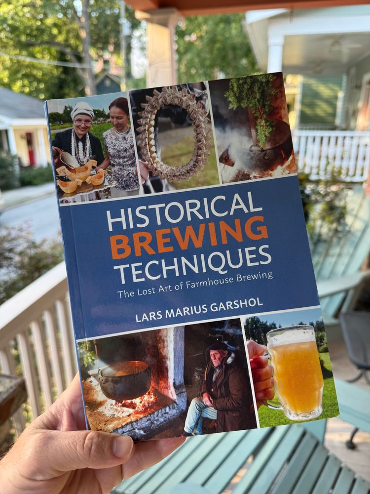 Photo showing a hand holding a copy of the book Historical Brewing Techniques by Lars Marius Garshol. In the background, a residential street in Raleigh, North Carolina 