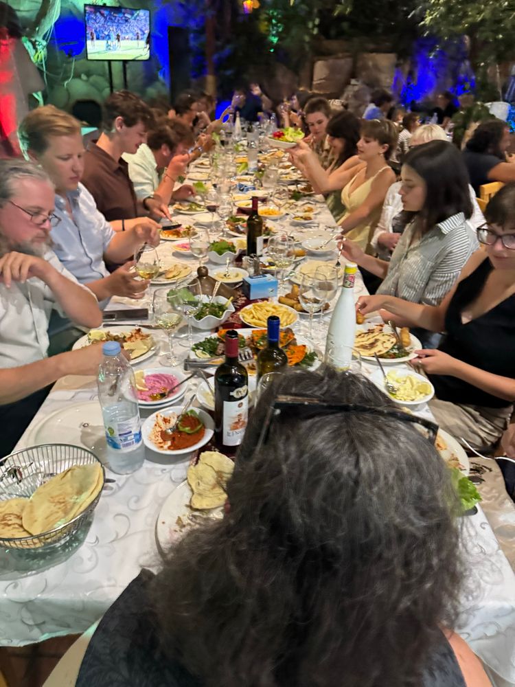Photo showing a group of students and archaeological field school staff sitting at a long table enjoying a Syrian meze 