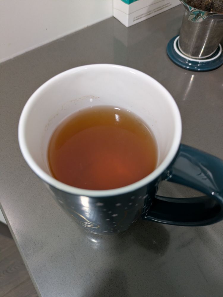 A teal mug full of a yellow-orange steeped tea.