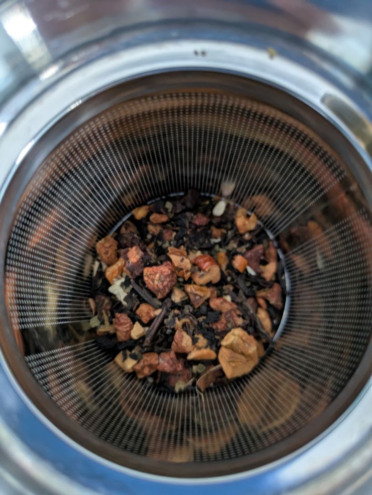 A close up shot of oolong loose leaf tea, nuts, and dried fruit in a mug.