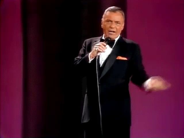 a man in a tuxedo and bow tie is singing into a microphone .