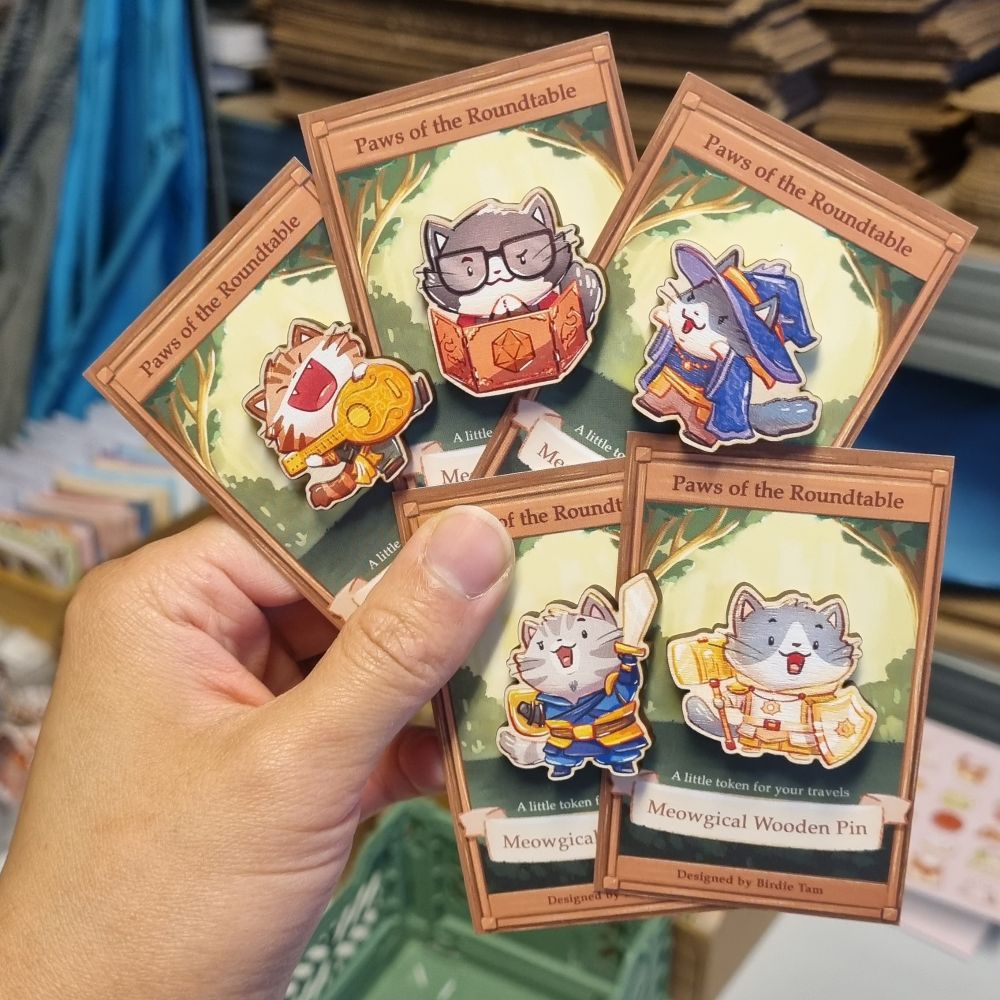 A photo of a hand holding small wooden pins of cats dressed up as fantasy characters 