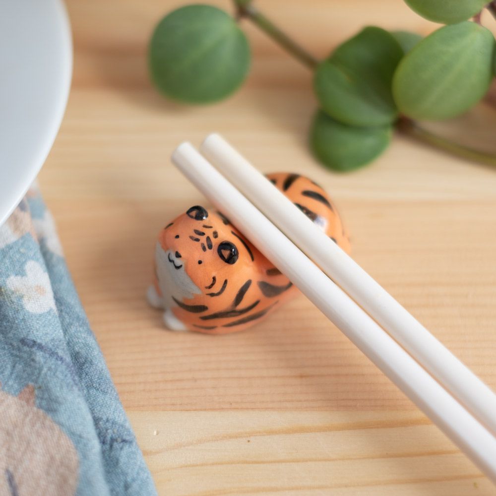 A photo of a small ceramic tiger with chopsticks resting on it
