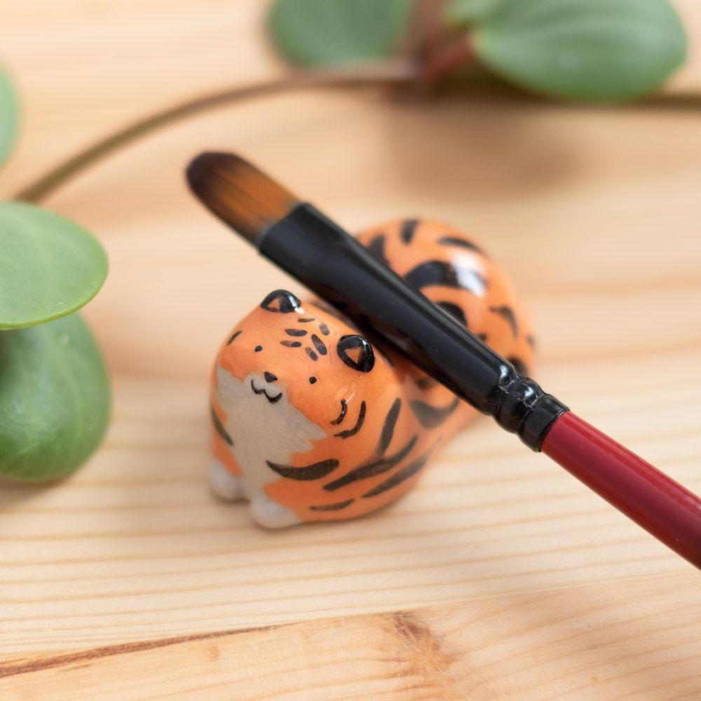 A photo of a small ceramic tiger with a paintbrush resting on it