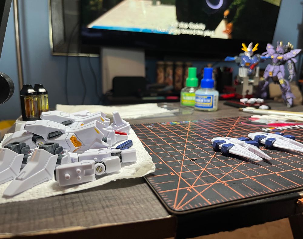 the remaining body pieces [minus the waist which needs to cure for a few more hours] for Gundam Odysseus laying in preparation for water slides. Gundam Odysseus’s torso and Varquil look on from the background next to Mr Mark setter/softer bottles. Godzilla plays in the background.