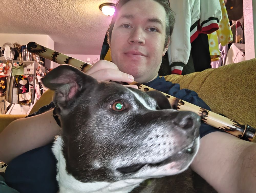 I'm holding a bamboo flute. A dog has managed to wedge herself between my arms.