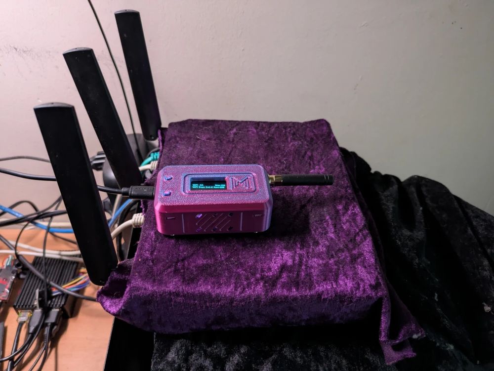 a router (covered in purple cloth) with three antennas, with the newly assembled LoRa unit on top
in the background a raspberry pi with all kinds of antennas sticking out of it
