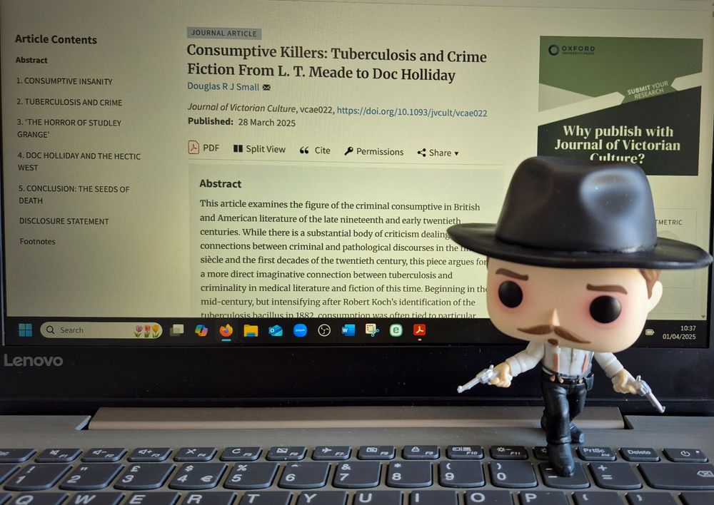 Image of article on a laptop screen with a tiny Doc Holliday doll in the foreground looking on approvingly.