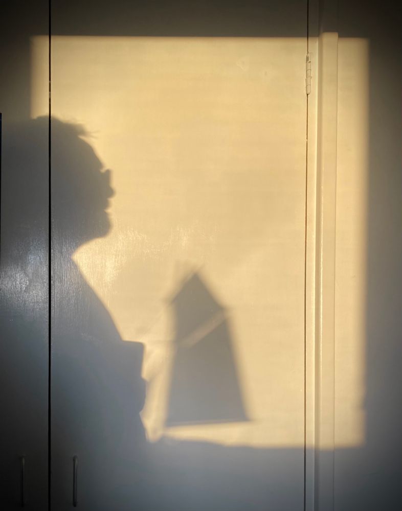 Sunrise shadow selfie with sailing ship. 
The dawn rises over the hills, casting a warm light on the wall, and the shadow of a model sailing boat which sits on the windowsill. I step into the frame and angle my iphone to capture a self portrait composition.