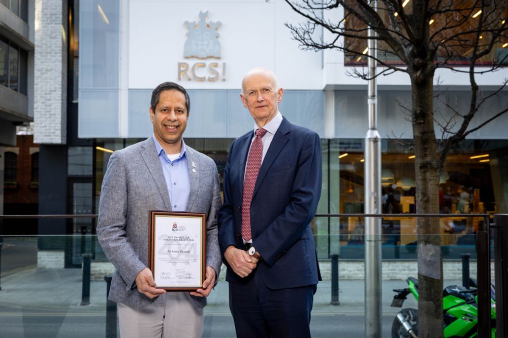 The photo shows a man receiving a framed award certificate titled "Vice Chancellor Innovation Awards 2025". He is pictured standing outdoors alongside a taller male figure in formal attire. Behind them is a RCSI building, clearly marked with its logo and crest.