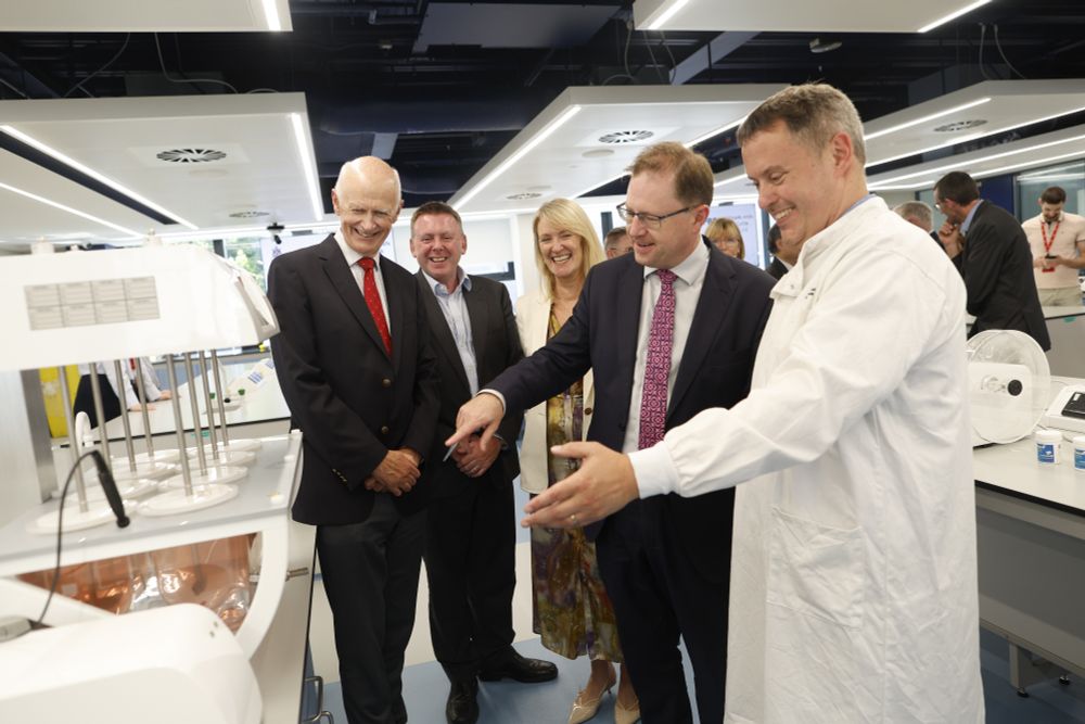 Minister James Lawless TD, wearing a dark suit and patterned tie, is welcomed during the official opening of newly refurbished laboratories at the RCSI School of Pharmacy and Biomolecular Sciences. He is pictured smiling alongside RCSI representatives and staff, including a researcher in a white lab coat, during a tour of the state-of-the-art teaching facilities. The group stands beside laboratory equipment in a modern, well-lit lab space.