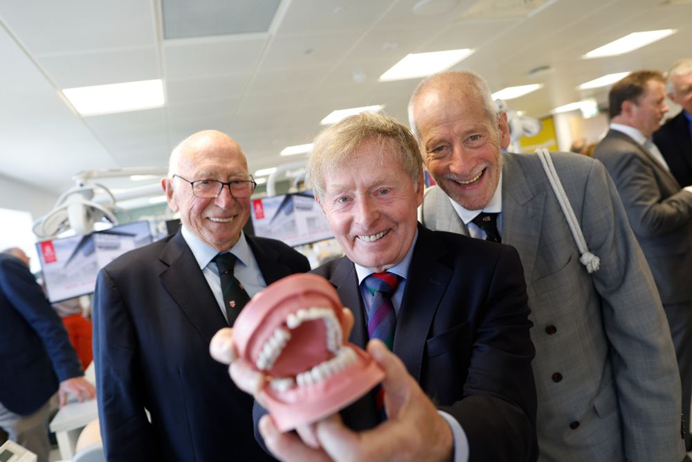 Three smiling guests, including alumni of the RCSI School of Dentistry, pose proudly with a dental model during the centre’s opening event. Background screens display visuals of the new Dental Education Centre.