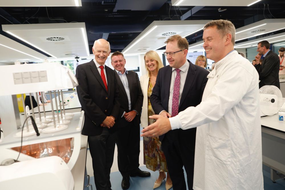 Minister James Lawless, wearing a dark suit and patterned tie, is welcomed during the official opening of newly refurbished laboratories at the RCSI School of Pharmacy and Biomolecular Sciences. He is pictured smiling alongside RCSI representatives and staff, including a researcher in a white lab coat, during a tour of the state-of-the-art teaching facilities. The group stands beside laboratory equipment in a modern, well-lit lab space.