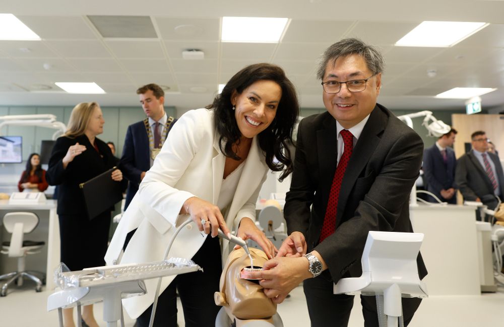 Minister Jennifer Carroll MacNeill and Professor Albert Leung, Head of the RCSI School of Dentistry, jointly operate dental tools on a mannequin in the simulation lab. The new RCSI Dental Education Centre is bustling with guests in the background.