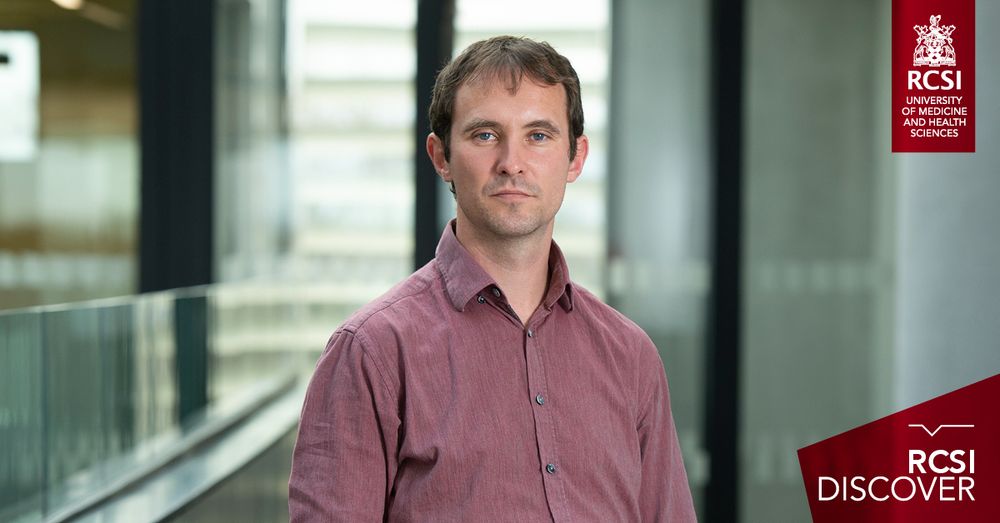 The image shows Professor Mick O'Reilly wearing a maroon button-up shirt, standing in a modern indoor setting with glass railings and blurred architectural details in the background. He has short brown hair and a neutral expression. The logo of RCSI appears in the top-right corner and "RCSI Discover" features in the bottom right corner.