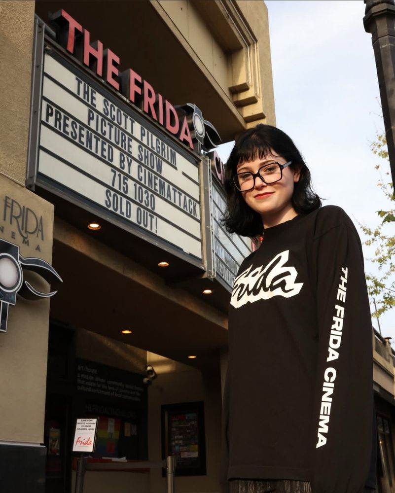 Woman modeling the new Frida long sleeve shirt in front of our marquee