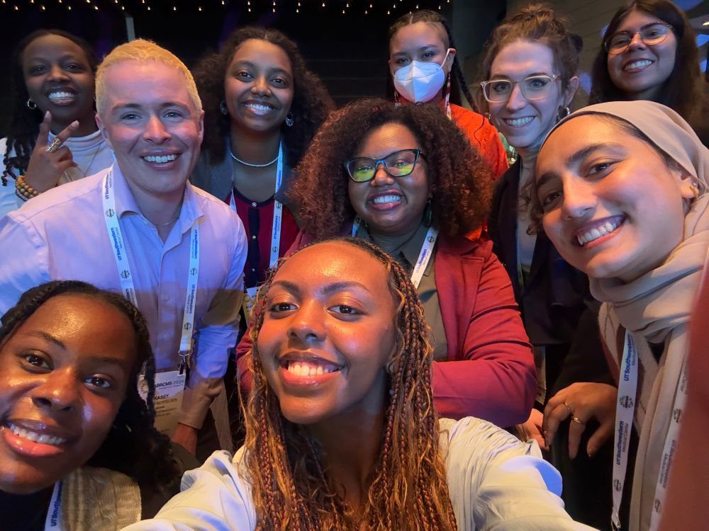 A group selfie of the 2024-25 cohort of MINDS post-baccalaureate scholars and their program director at the 2024 ABRCMS conference. This diverse group of historically marginalized scholars are all dressed up in conference attire and smiling widely for the photo.