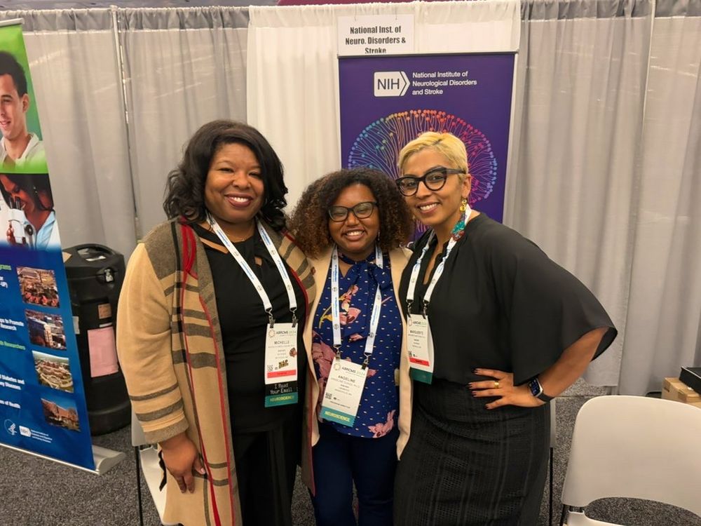 Three Black women DEI leaders smiling and hugging each other while taking a group photo. Dr. Jones-London on the left has curled short hair and is wearing a black outfit with a long brown plaid pattern cardigan. Dr. Dukes in the middle has a curly Afro and is wearing a dark blue blouse with pink flowers and gold dots with a light pink blazer on top. Dr. Matthews on the right has a short blonde haircut and is wearing a black blouse and skirt with colorful big earrings.