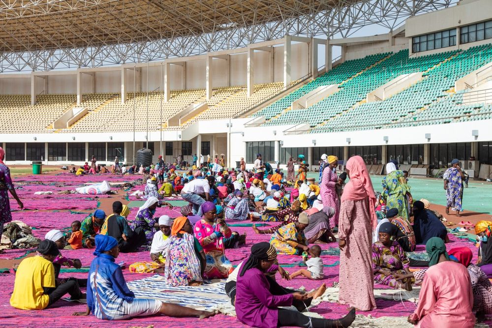 dozens of people gather to in a stadium to sew textiles