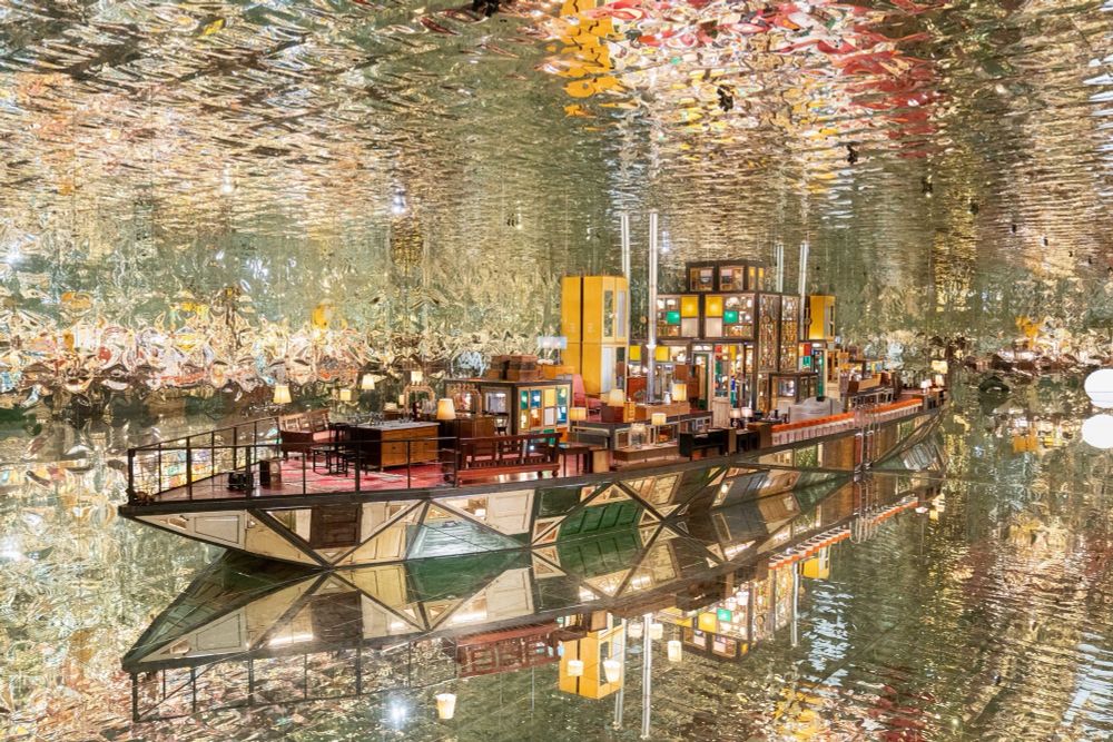 a large-scale installation by Song Dong in the shape of a boat within a fully reflective room, using found wooden window frames, color-coated glass, lamps, furniture, and other knick-knacks