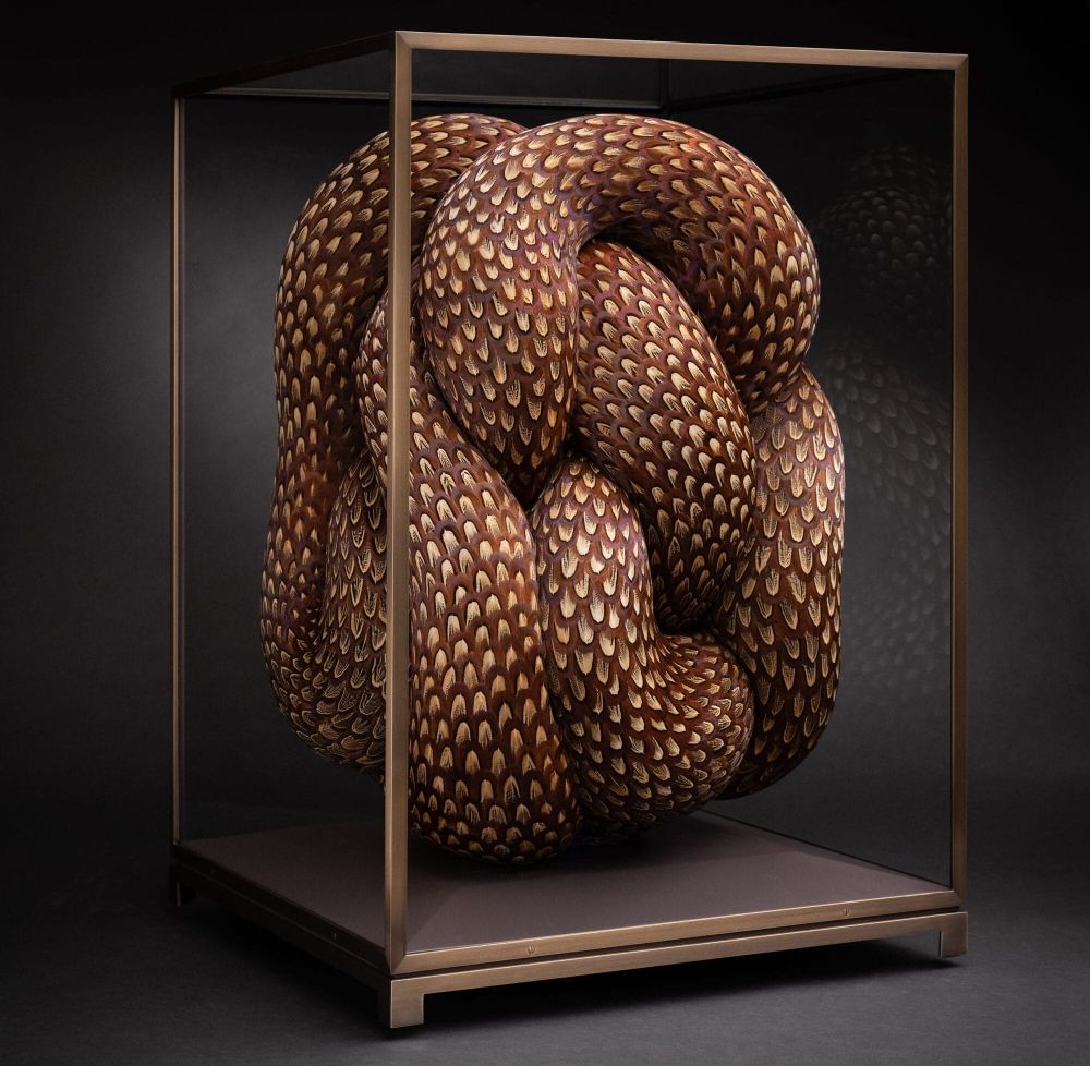 a sculpture made of patterned feathers that appear to be serpentine and knotted inside of a glass vitrine