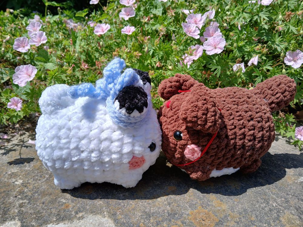 round crochet white bunny and brown puppy touching noses in front of small pink flowers