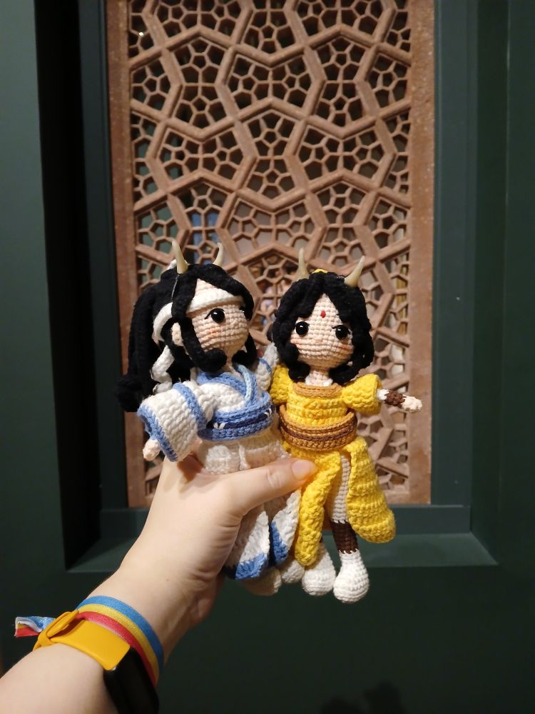 Crochet dolls of Lan Sizhui and Jin Ling held up in front of a carved stone window