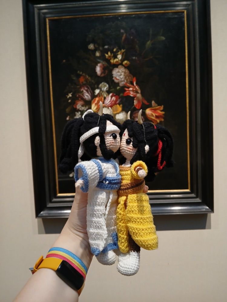 Crochet doll of Jin Ling kissing crochet doll Lan Sizhui on the cheek in front of a still life oil painting of flowers
